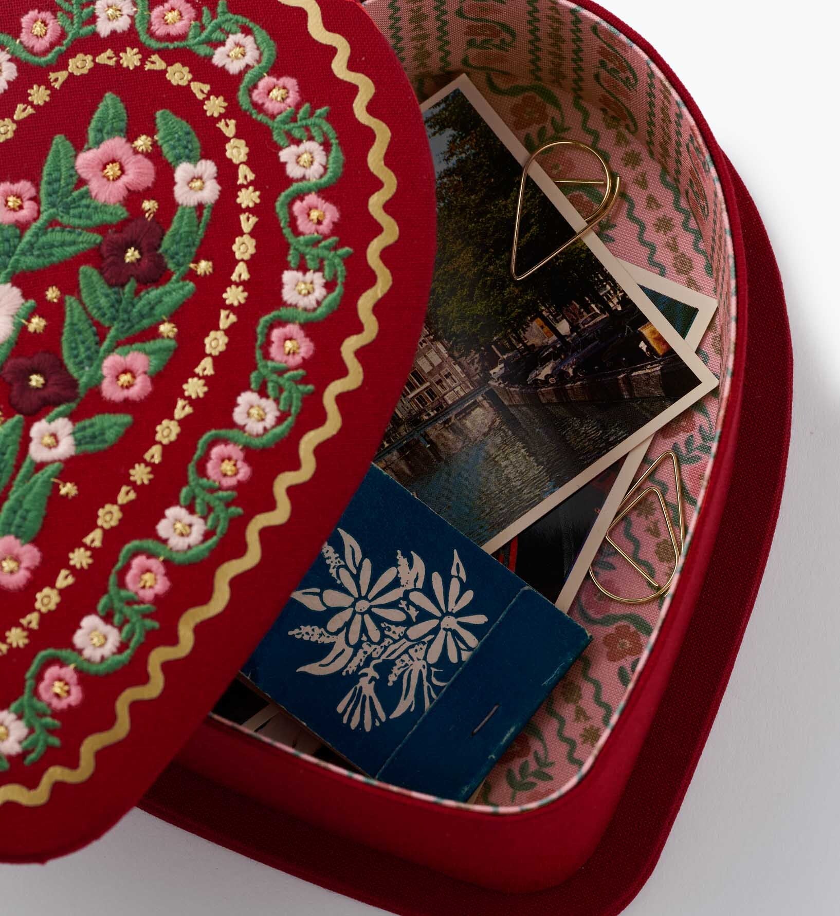 Decorative red box with floral embroidery, a blue card, and photos inside.